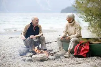 Älteres Paar sitzt am Lagerfeuer und grillt Fisch