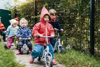 Copii care folosesc scutere în grădina unei grădinițe