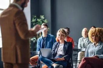 Grup de bărbați și femei care ascultă un seminar. Ei zâmbesc.