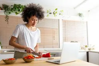 moteris gamina maistą pagal internetinį receptą naudodama nešiojamąjį kompiuterį