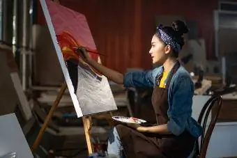 Wanita duduk di depan lukisan besarnya di atas kanvas