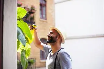 jong man wat sy plante op sy balkon natmaak