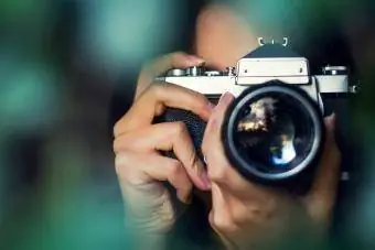 Fotógrafo de mulher fotografando com uma câmera analógica entre folhas de árvores ao pôr do sol