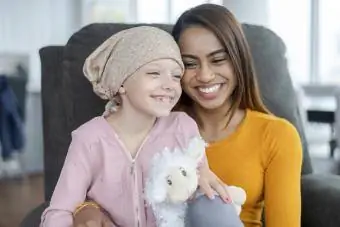 Syöpää sairastava nuori tyttö istuu äitinsä sylissä