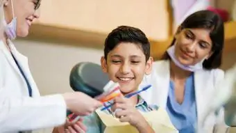 Masayang batang lalaki na pumipili ng toothbrush at nakangiti sa isang dental clinic