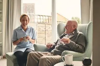 Burrë i moshuar dhe kujdestare femër duke shijuar kafenë në shtëpi