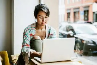 Jonge vrouw die op laptop werkt in cafévenster