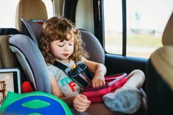 Giovane ragazza seduta su un seggiolino per auto e pranzando durante un viaggio