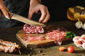 Mãos de mulher cortando salsicha de salame na placa de madeira