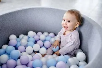 Seorang bayi perempuan sedang duduk di dalam timbunan bola berwarna-warni warna pastel