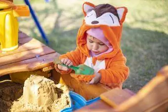 Roztomilé batoľa v oranžovej kombinéze sa hrá v piesku