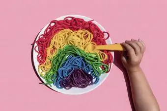 Кемпірқосақ түсті спагетти жеп жатқан қыздың қолы