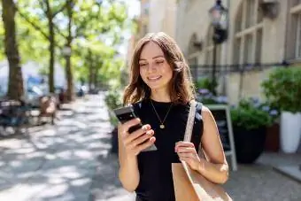 Người phụ nữ trẻ mỉm cười với chiếc điện thoại thông minh đang đi trên phố