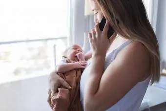 Mor holder nyfødt baby og har en telefonsamtale