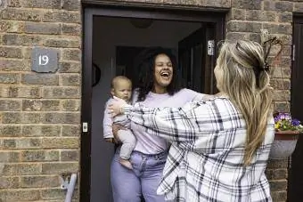 ibu menggendong bayinya sambil berdiri di ambang pintu