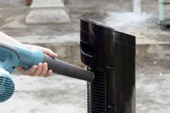 Oseba uporablja puhalo za čiščenje stolpnega ventilatorja