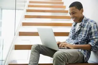 Подросток пользуется ноутбуком на ступеньках дома
