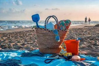 Strandsak met voorwerpe, bril, handdoek, graaf, flip-flops, boek ens daardie oppervlak, gelê op die strand teen sononder