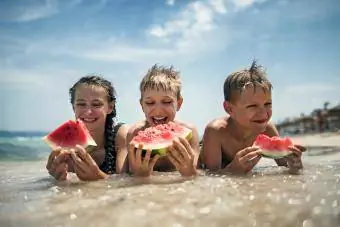 ბედნიერი ბავშვები საზამთროს ჭამენ სანაპიროზე