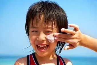 Mãe aplicando protetor solar em criança na praia