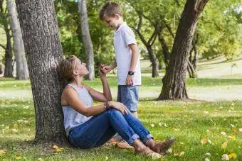 Anya farmert és kényelmes felsőt visel, miközben a parkban játszik a fiával