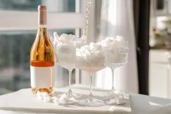 یک بطری شراب گازدار گل رز مایع با لیوان و آب نبات پنبه