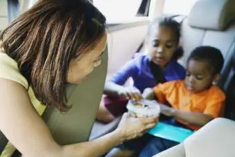 Mama pomáha svojim deťom usadiť sa v aute a dáva im občerstvenie
