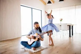 tēvs un mazā meita ar ģitāru iekštelpās mājās, izklaidējas
