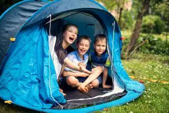 Дети счастливо сидят внутри синей палатки