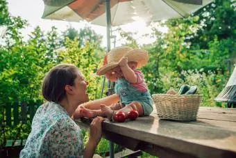 Blide mor og datter koser seg ute mens babyen prøver morens hatt.