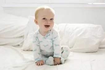 Sevimli bebek çocuk yatağın üstüne oturmuş gülümsüyor
