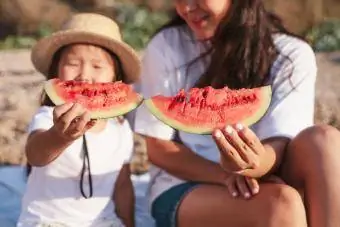 Matka a dcera jíst meloun a bavit se na pláži