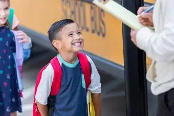 Susijaudinęs pradinės mokyklos berniukas sveikina autobuso vairuotoją, kai jis ruošiasi krauti autobusą