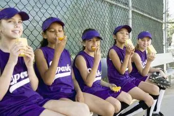 Spelers uit de Little League drinken sapdozen en eten sinaasappel