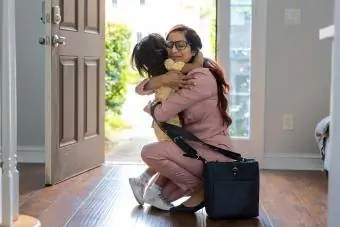 Kleinkind umarmt Mutter im Türrahmen, als sie von der Arbeit nach Hause kommt