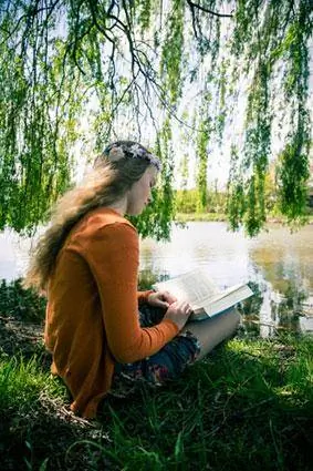 Adolescente con libro sentado bajo el sauce llorón