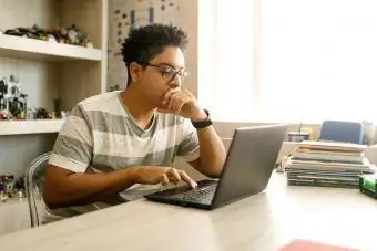 Tienerjongen die aan bureau op laptop bestudeert