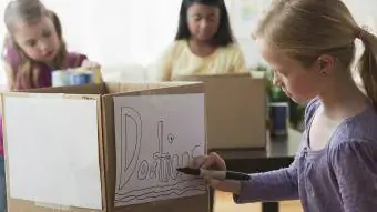 Menina desenhando sinal de doação em caixa de papelão