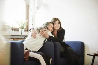 Mama și fiica adolescentă se îmbrățișează în timp ce stau pe scaune