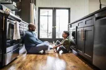 tētis un dēls sēž virtuvē uz grīdas un pārdomāti sarunājas
