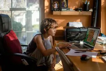 Seorang anak laki-laki praremaja duduk di depan komputer memainkan permainan catur online