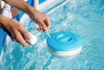 Verificarea calității apei dintr-o piscină cu ajutorul unei benzi de test cu valoarea PH, clor și algicid
