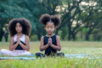 сладки деца, които медитират върху постелка за йога на открито
