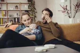Mamma och pappa gosar bebis medan pappa gäspar