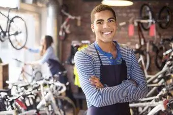 Nastoletni pracownik sklepu rowerowego stoi dumnie przed swoim asortymentem