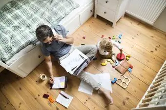 ayah sedang bekerja sambil duduk di samping anak yang sedang bermain