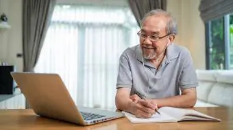 oudere man leert op zijn laptop en maakt aantekeningen