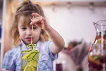 Kleines Mädchen trinkt Wasser mit Zitrone und Gurke