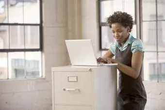 Nainen työskentelee kannettavalla tietokoneella arkistokaapissa