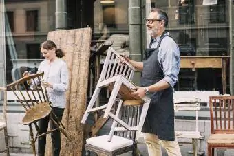 Мужчина расставляет деревянные стулья в антикварном магазине